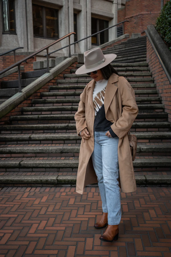 Woman in trench coat and hat walking on brick walkway in fall weather