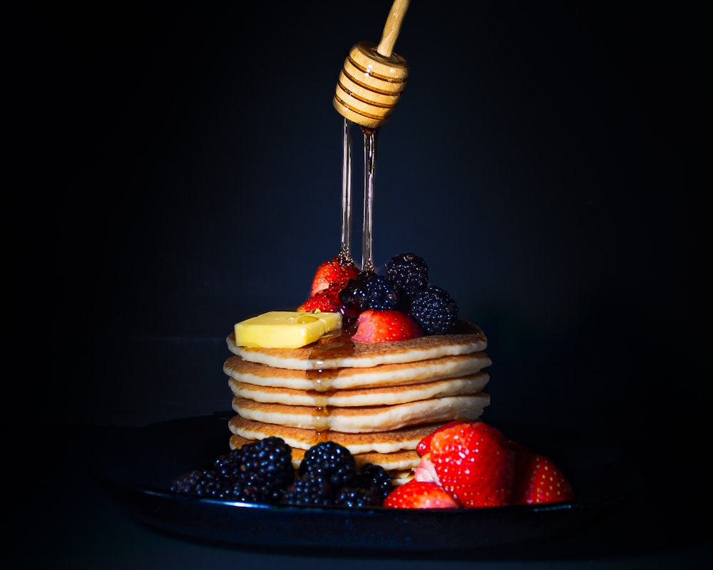 a stack of pancakes topped with fruit and honey