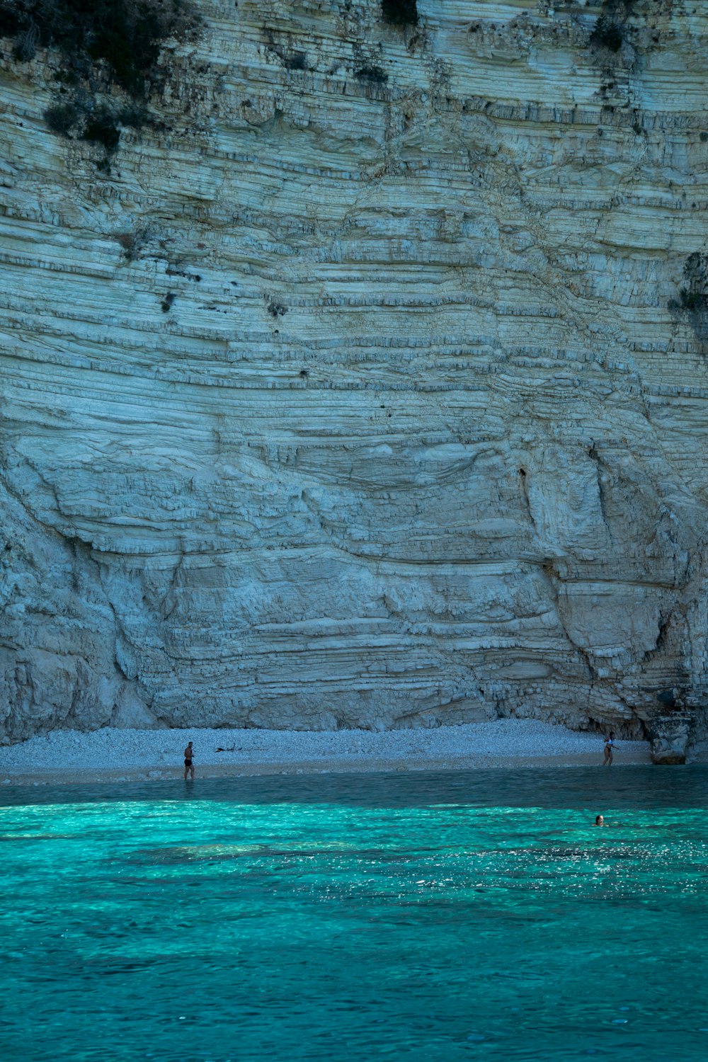 a group of people standing on a beach next to a cliff