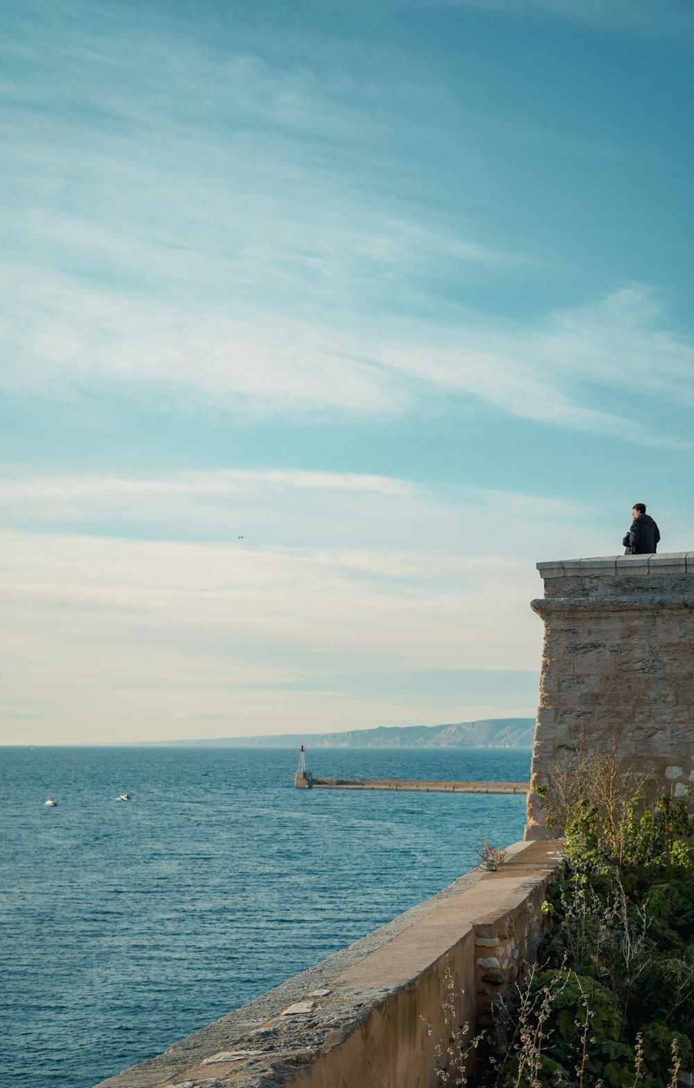 Una persona sentada en una repisa con vista al océano