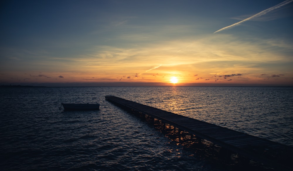 o sol está se pondo sobre o oceano com um barco na água