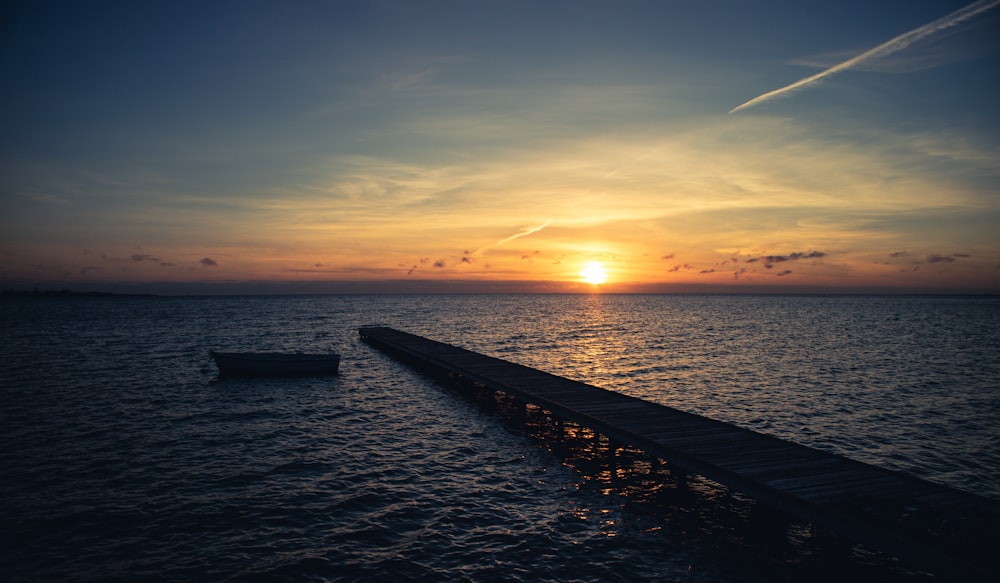 the sun is setting over the ocean with a boat in the water