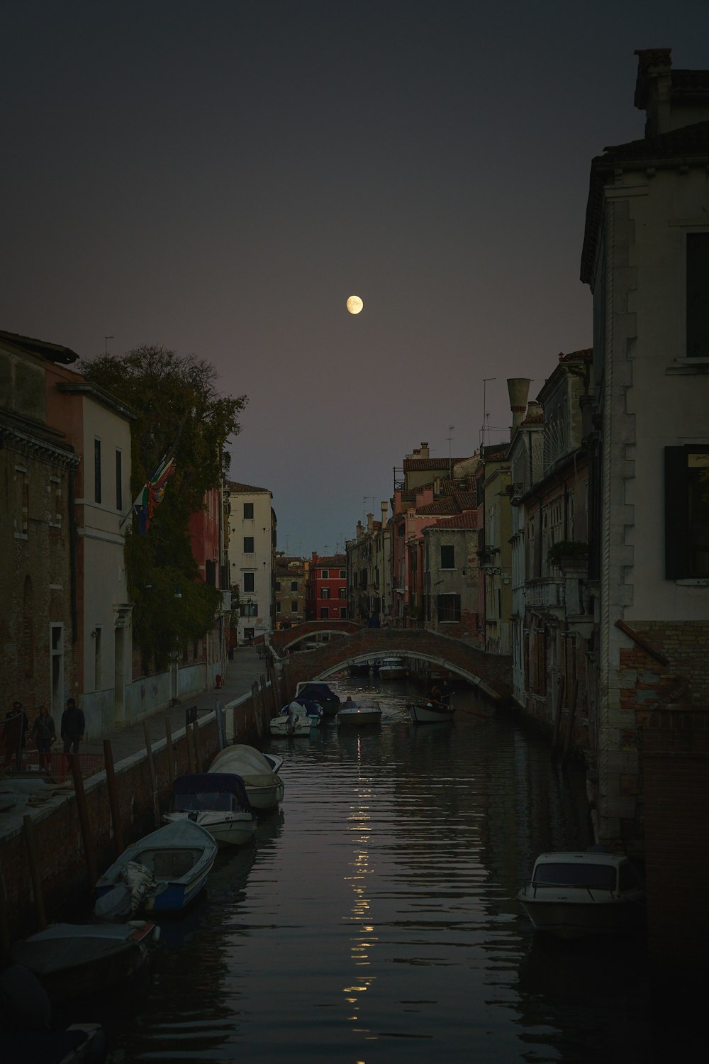 a full moon rises over a canal in a city