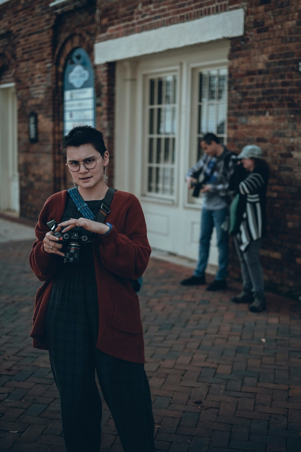 Eine Frau steht vor einem Backsteingebäude und hält eine Kamera in der Hand
