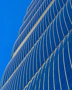A sleek, glass-fronted office tower reflecting the Dubai skyline under a bright blue sky.
