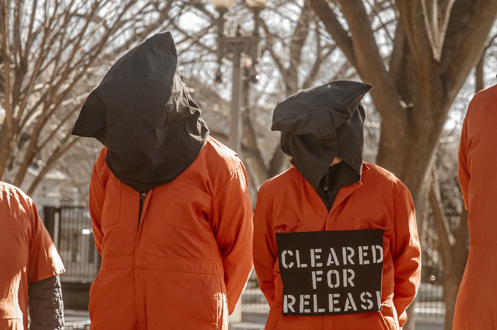 Un groupe de personnes en combinaison orange avec une pancarte sur laquelle on peut lire Cleared for