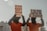 Two individuals dressed in orange jumpsuits and hoods are holding protest signs. One sign reads '20 Years of Disgrace Close Guantanamo' and the other says 'I Am Dying Waiting for Justice'. They are chained and standing outside a significant government building.
