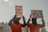 Two individuals dressed in orange jumpsuits and hoods are holding protest signs. One sign reads '20 Years of Disgrace Close Guantanamo' and the other says 'I Am Dying Waiting for Justice'. They are chained and standing outside a significant government building.
