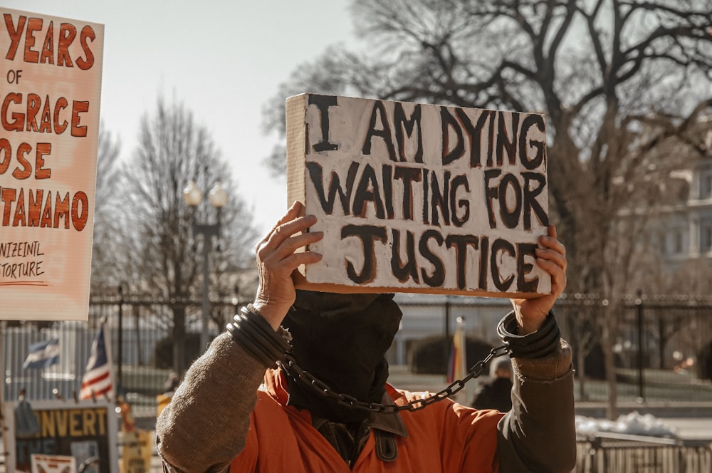a man holding a sign that says i am dying waiting for justice