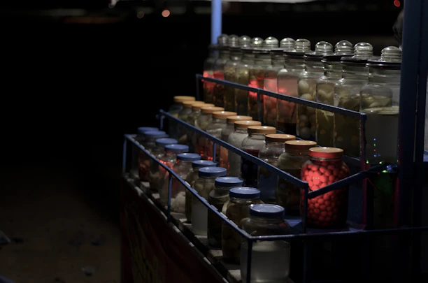 Close-up of hands organizing jars of preserved food on wooden shelves with warm brown tones.