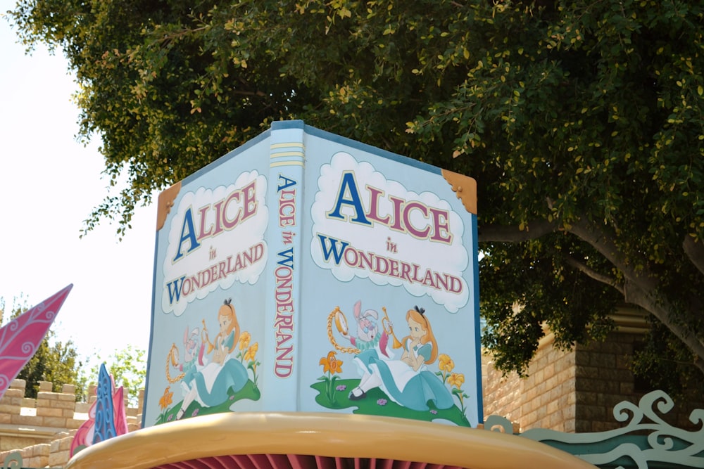 a sign for alice and the wonderland land in front of a tree