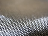 A close-up view of a textured woven fabric featuring a grid-like pattern with shiny, metallic-looking fibers.