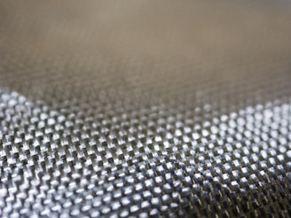 A close-up view of a textured woven fabric featuring a grid-like pattern with shiny, metallic-looking fibers.