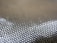 A close-up view of a textured woven fabric featuring a grid-like pattern with shiny, metallic-looking fibers.
