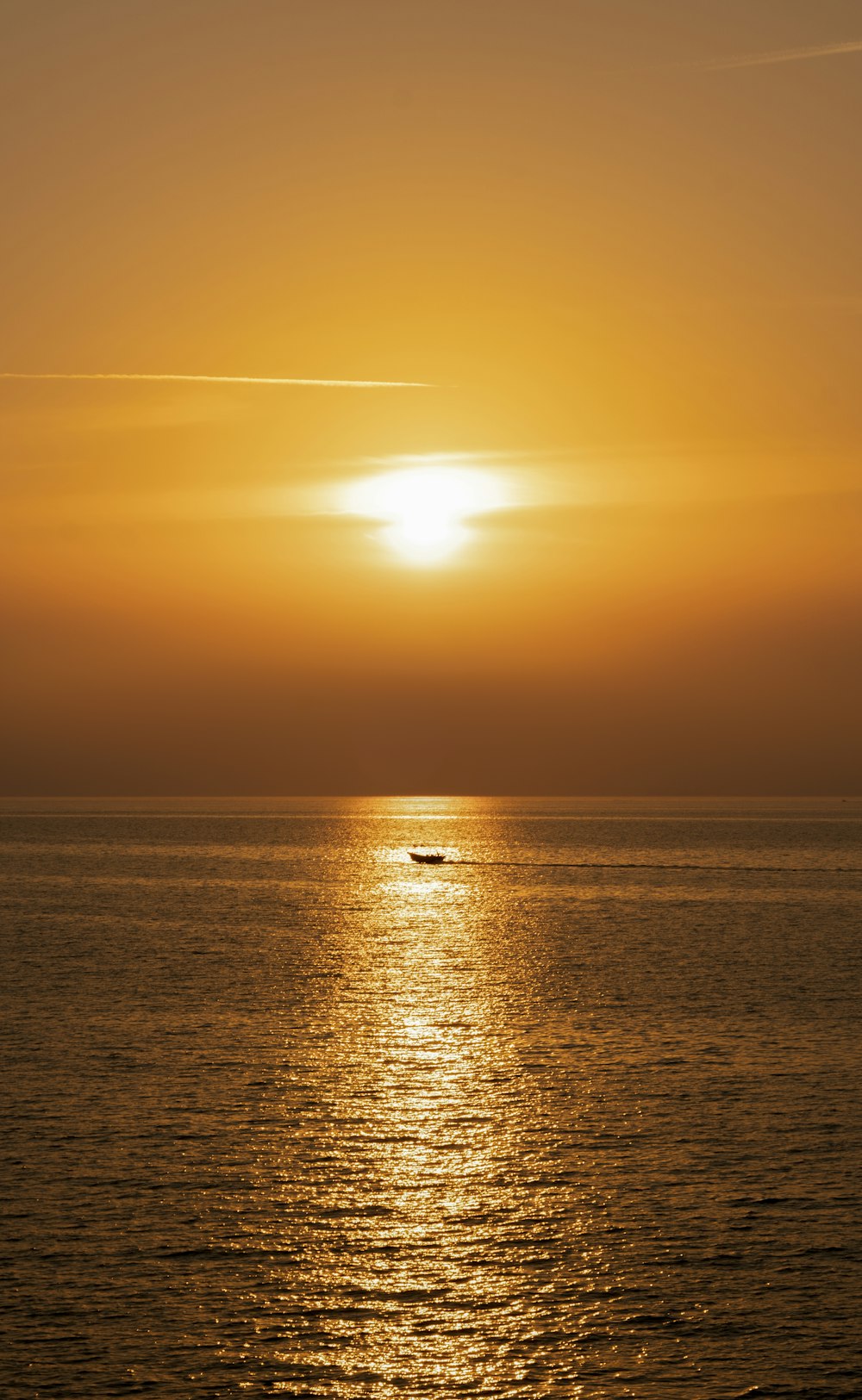 the sun is setting over the ocean with a boat in the water