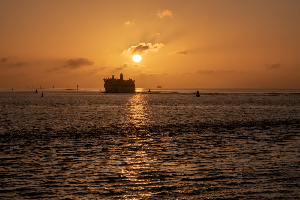 the sun is setting over the ocean with a ship in the distance