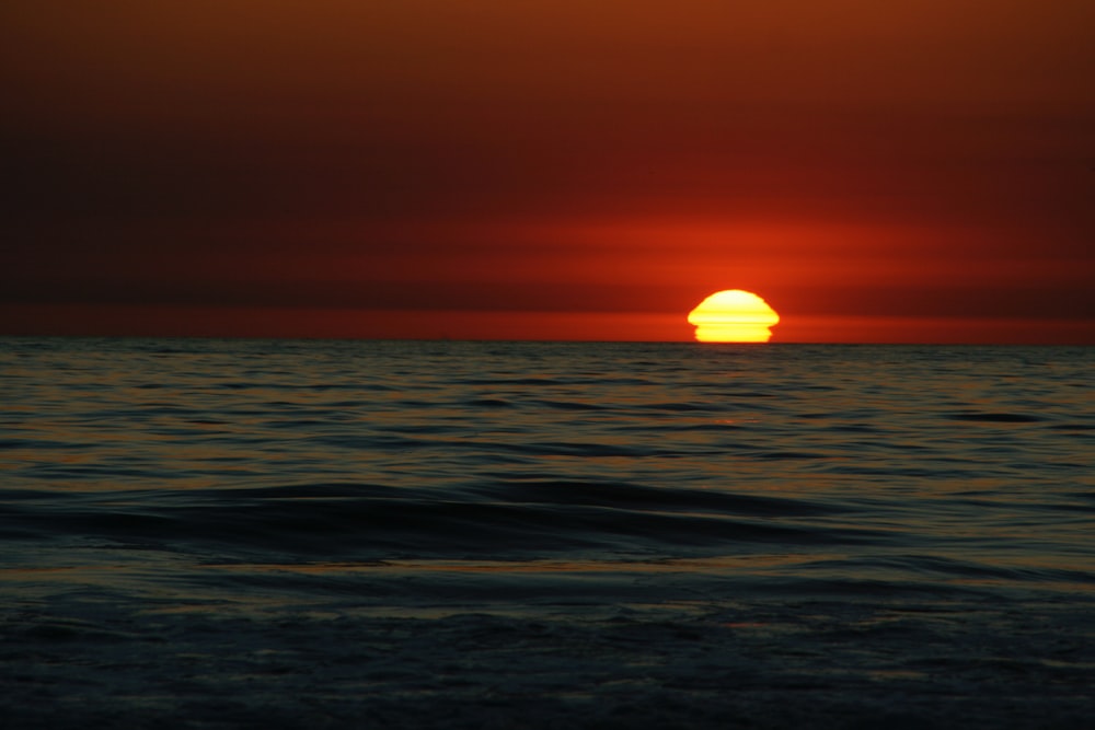 the sun is setting over the ocean on a cloudy day