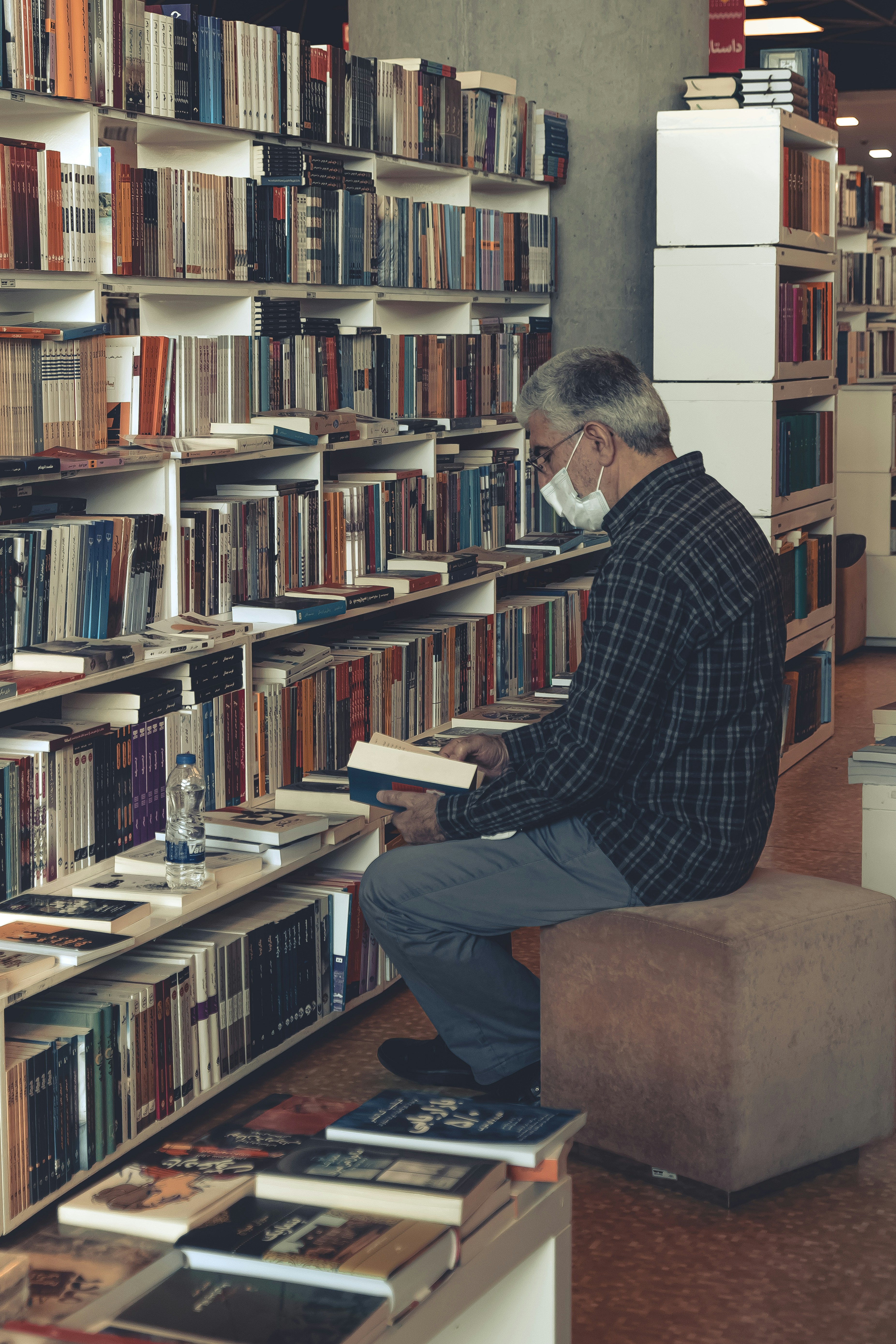 um homem sentado em um banquinho na frente de uma estante