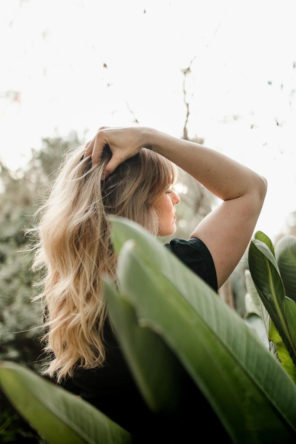 a woman with long blonde hair standing next to a plant