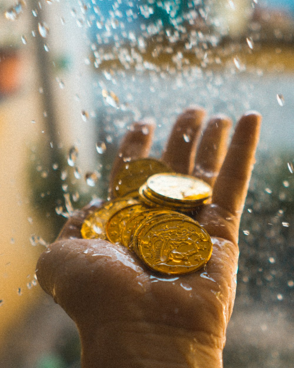 a hand holding a gold coin in front of a window