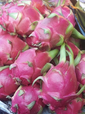 A collection of vibrant pink dragon fruits with green leafy tips is piled together, showcasing their unique texture and thorns. The fruit's surface is smooth and glossy, emphasizing the freshness and ripeness.