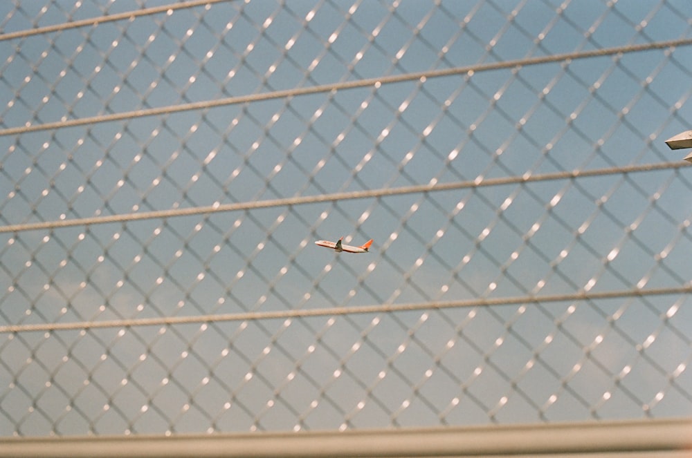 a small plane flying by a chain link fence