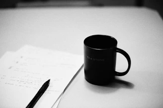 a black coffee mug sitting on top of a table next to a pen