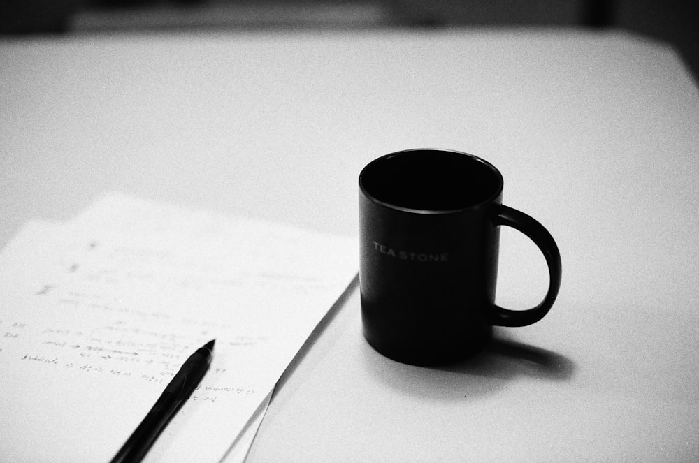 a black coffee mug sitting on top of a table next to a pen
