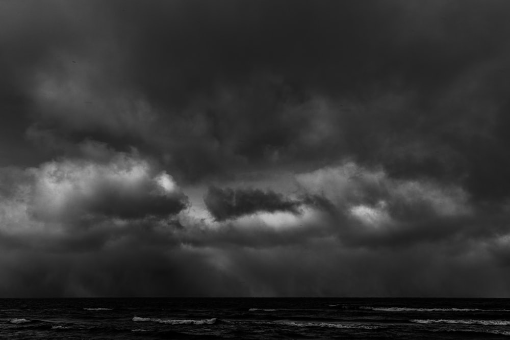 a black and white photo of storm clouds over the ocean