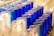 Rows of cylindrical glass candle holders in blue and white, some of which contain lit candles. The overall arrangement suggests a prayer or memorial setting.
