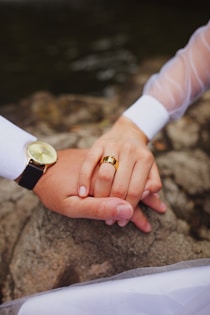 Close-up of intertwined hands adorned with subtle gold jewelry, hinting at a sensual connection.