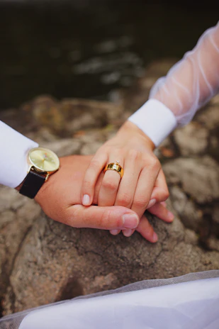 A joyful couple holding hands, showcasing their matching wedding rings in natural light.