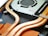 Close-up view of the internal components of an electronic device, featuring copper heat pipes, a cooling fan, and circuit board parts. The image highlights the intricate design and arrangement of these components.