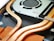 Close-up view of the internal components of an electronic device, featuring copper heat pipes, a cooling fan, and circuit board parts. The image highlights the intricate design and arrangement of these components.