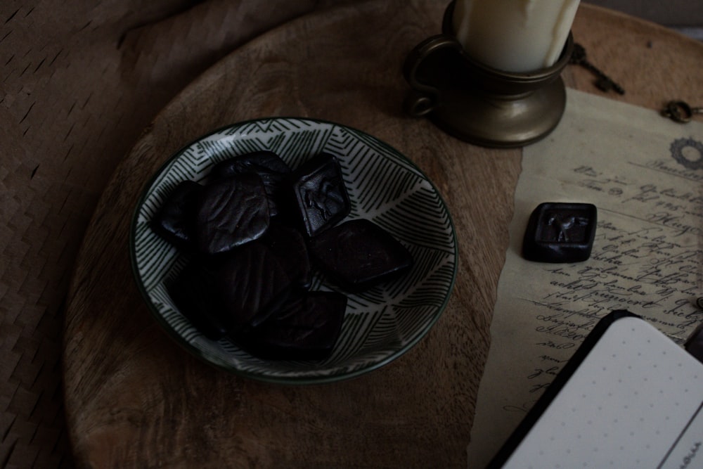 a glass bowl filled with dark chocolates next to a notebook