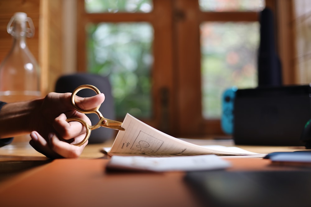 a person holding a pair of scissors over a piece of paper