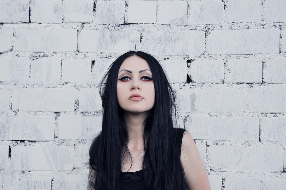 a woman with long black hair standing in front of a brick wall