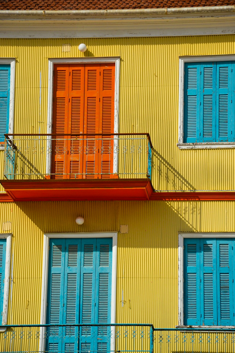 a yellow building with blue shutters and a red balcony