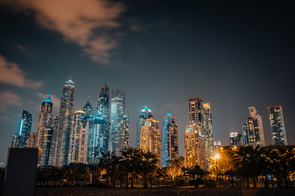 a night view of a city with skyscrapers and palm trees