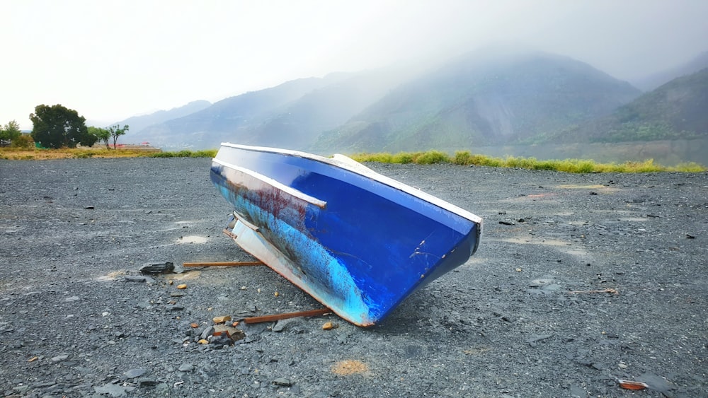 a blue boat sitting on top of a gravel field