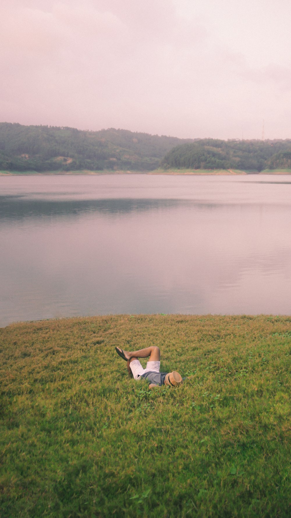 a man laying in the grass next to a body of water