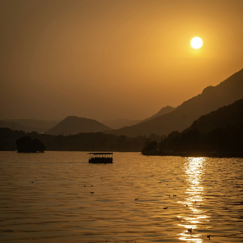 a small boat floating on top of a lake at sunset