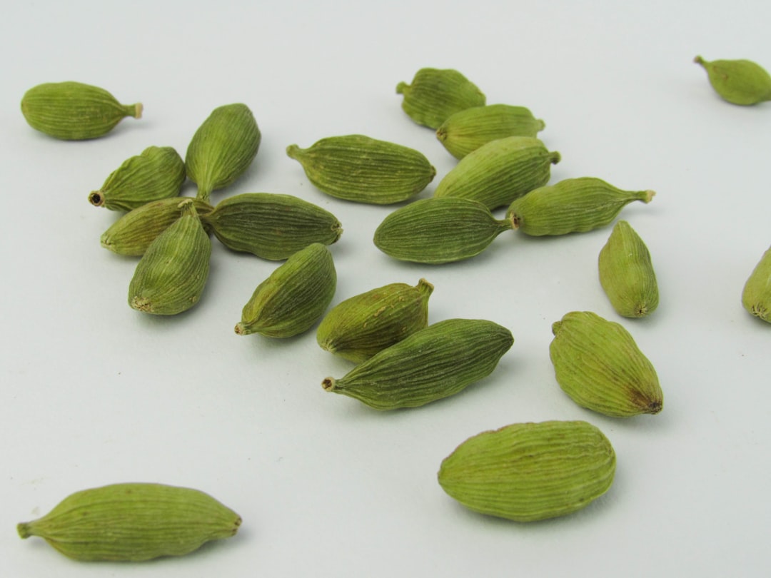 a pile of green cardamoa seeds on a white surface, Cardamom on a white background