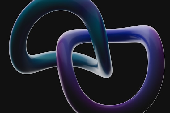Two interconnected, glossy, ribbon-like loops with a smooth, reflective surface. The loops feature a gradient of colors including purple, blue, and teal, set against a dark background.