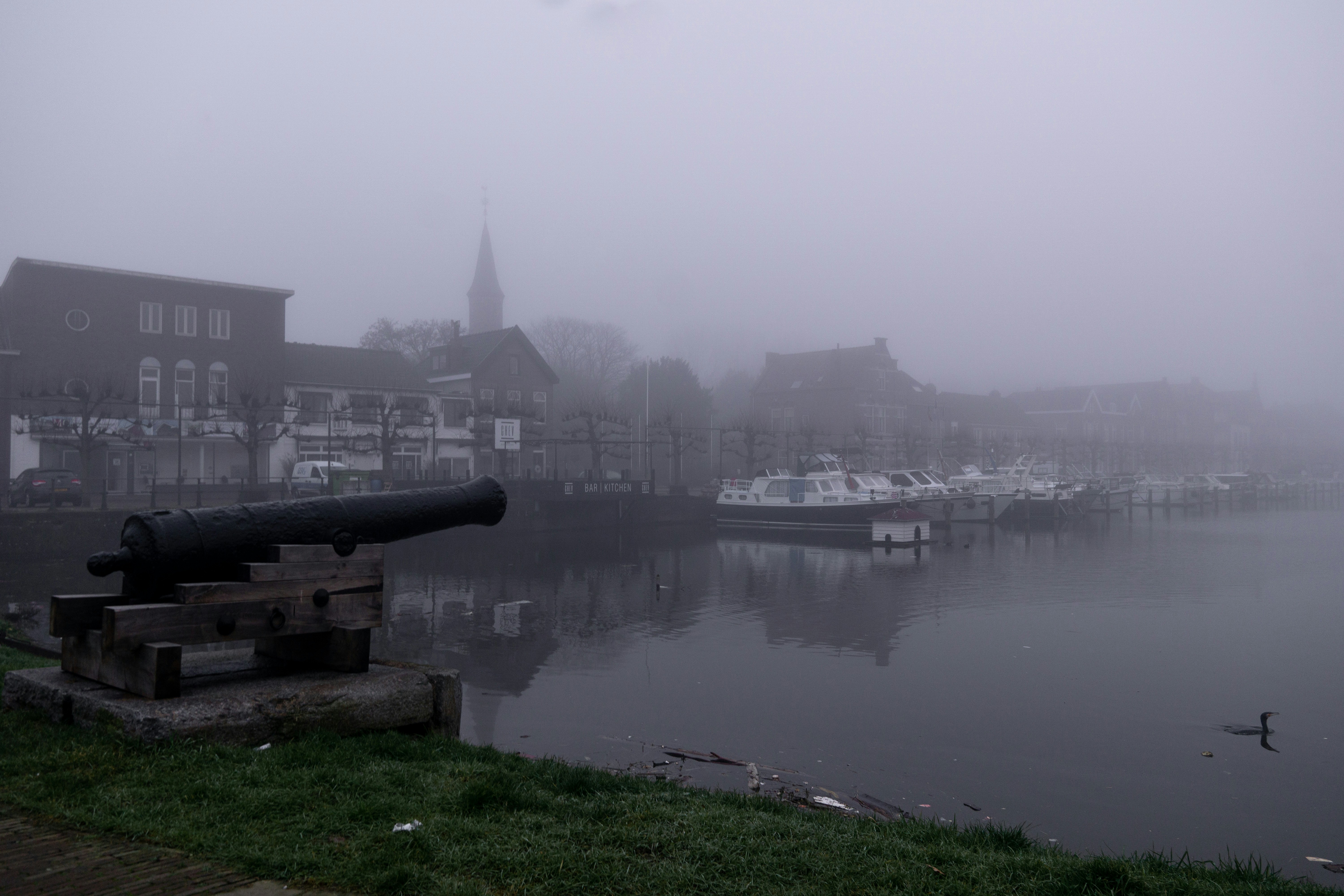 a foggy harbor with boats and a cannon
