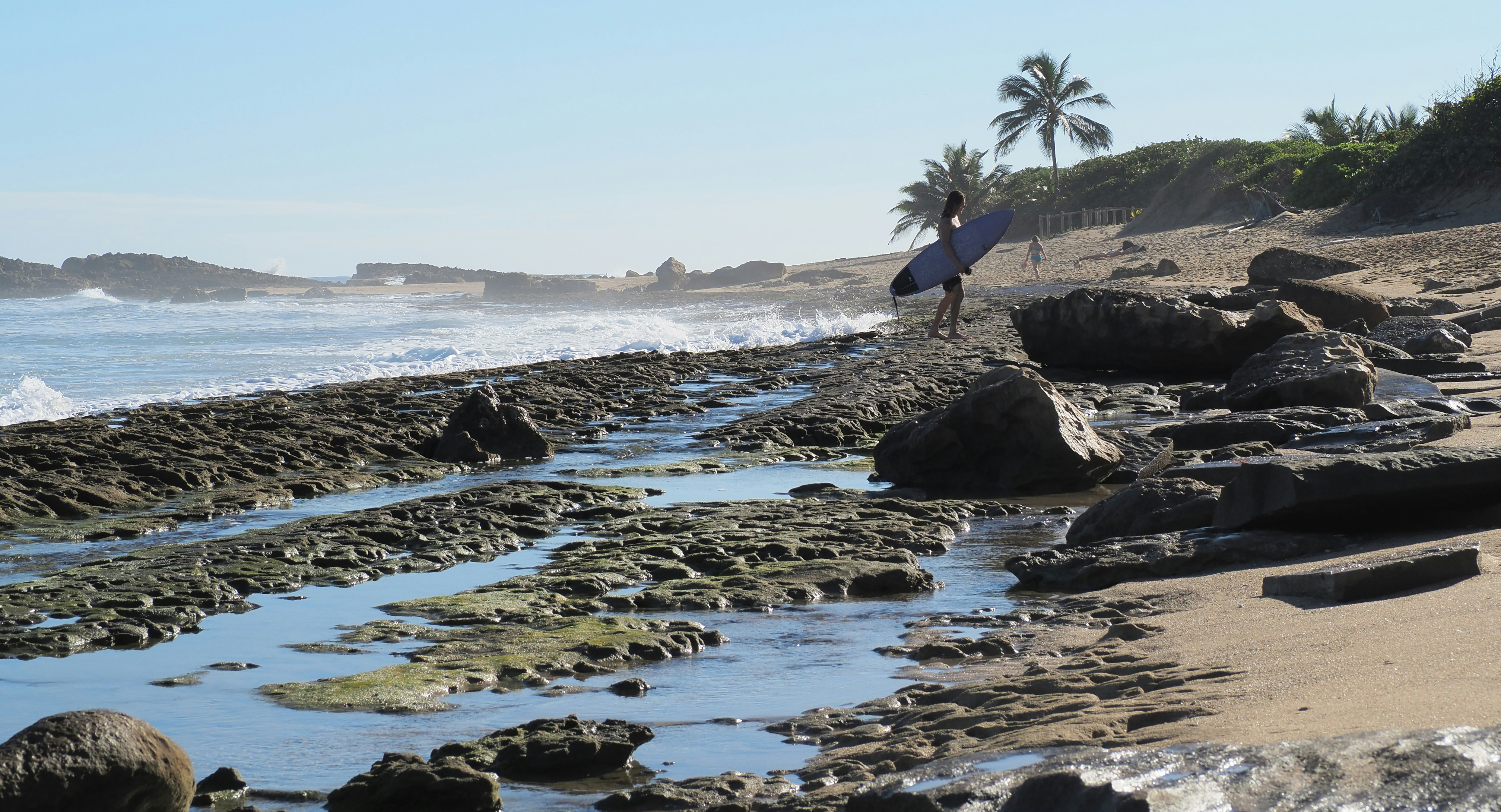 a person carrying a surfboard on a rocky beach