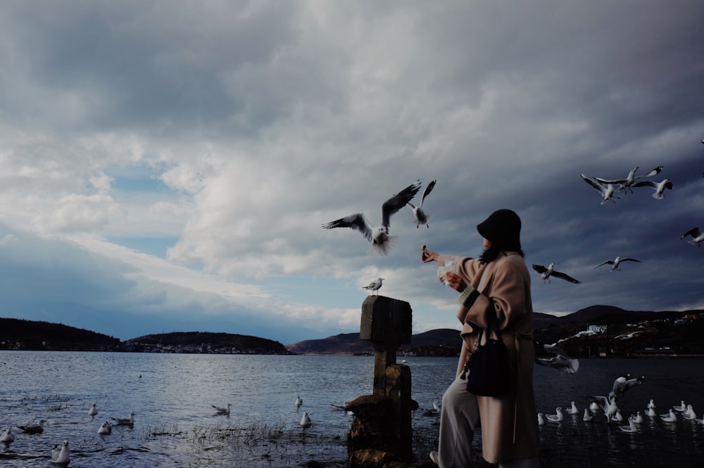 a woman standing on a pier feeding seagulls