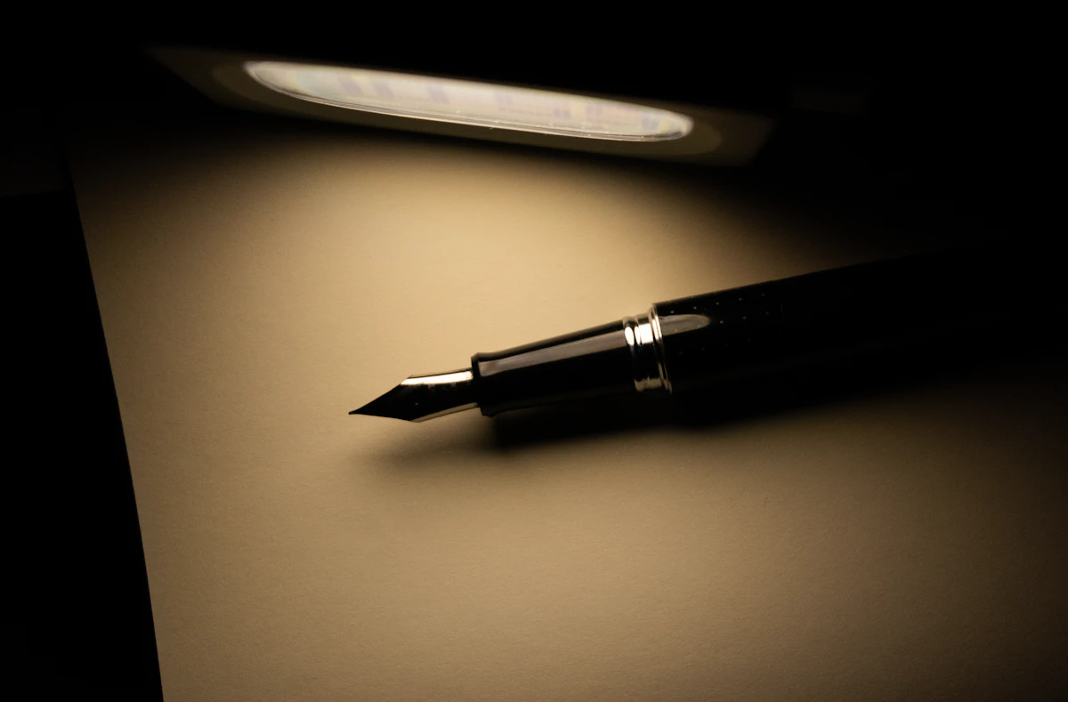 A fountain pen resting on a blank sheet of paper under a desk lamp