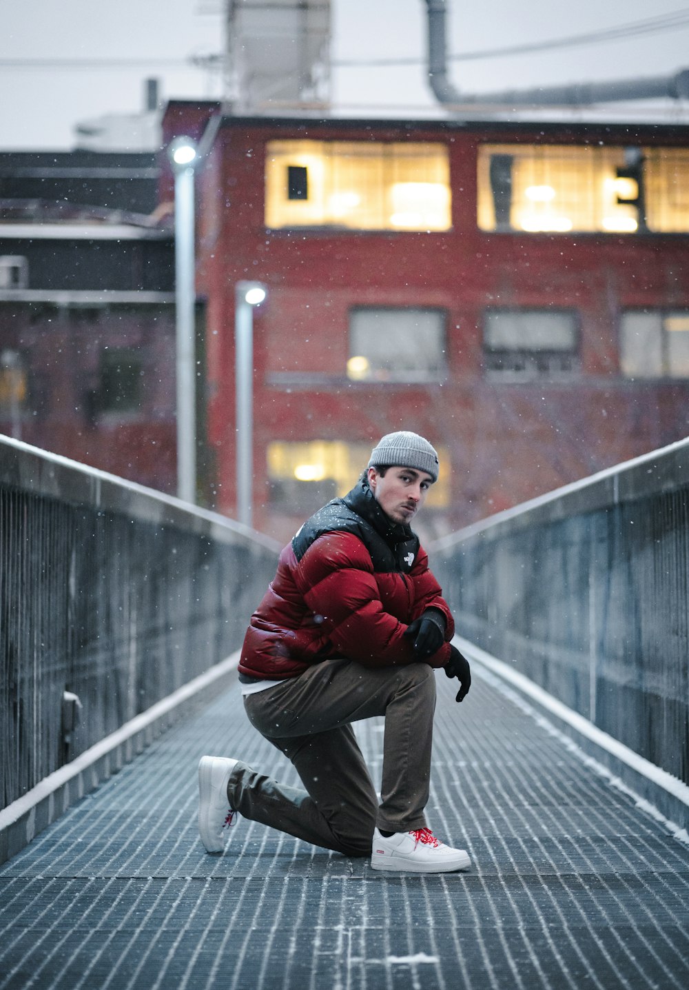 a man squatting down on a bridge in the snow