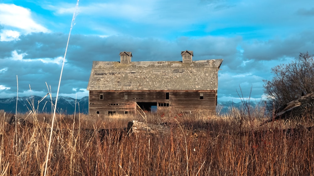 uma antiga casa abandonada em um campo com montanhas ao fundo